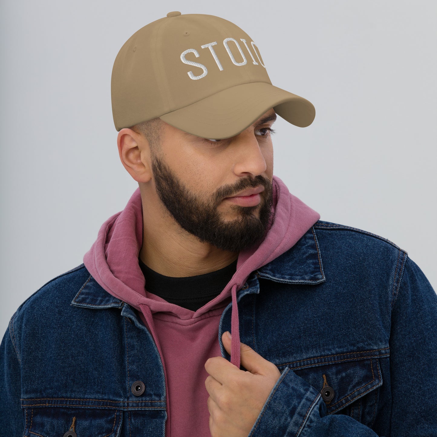 Man wearing beige Stoic embroidered dad hat, pink hoodie, and denim jacket