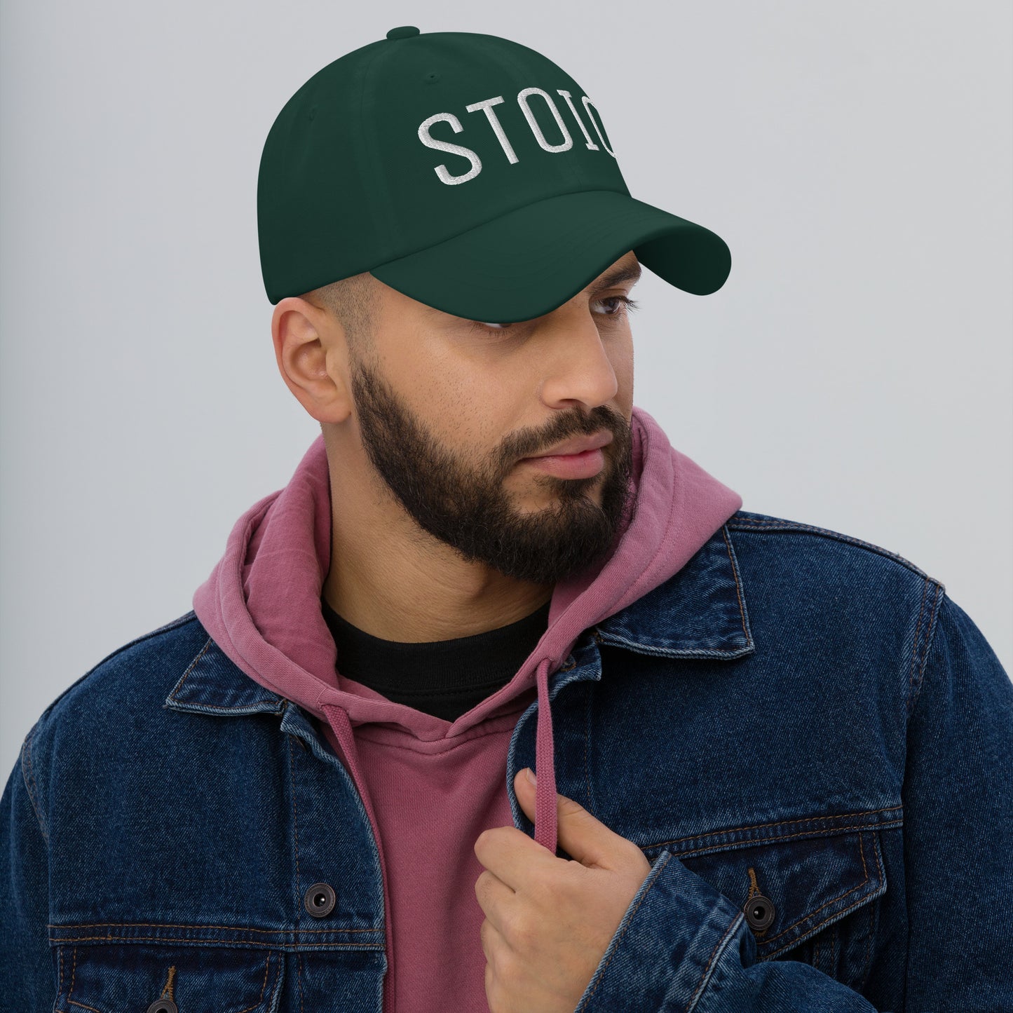 Man wearing a green dad hat with "STOIC" embroidered, casual streetwear style with a pink hoodie and denim jacket