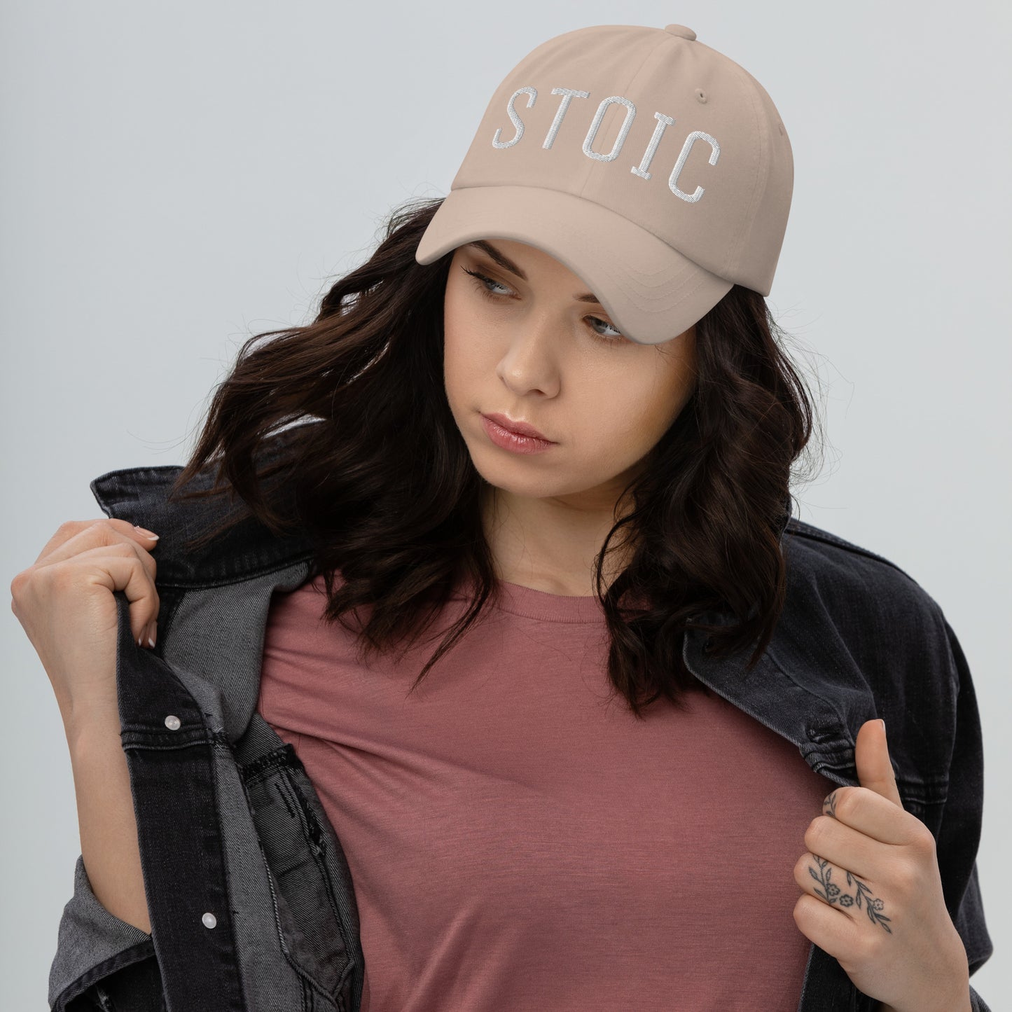 Beige embroidered dad hat with "STOIC" text worn by a woman in a denim jacket and pink t-shirt